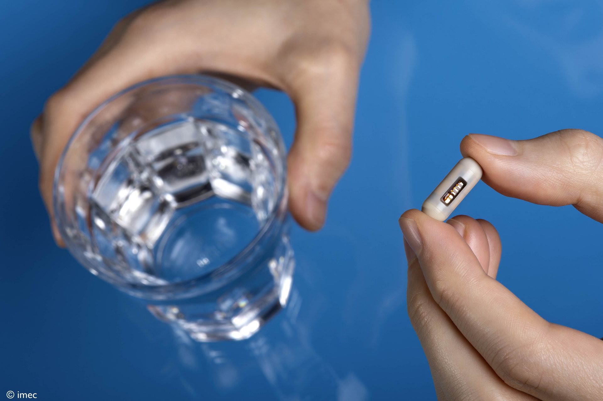 The GutOS capsule prototype held between two fingers next to a glass of water